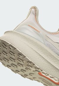 White textured running shoe with a padded collar, distinctive striped accents, and a patterned outsole. Features "ULTRABOOST" branding and orange details.