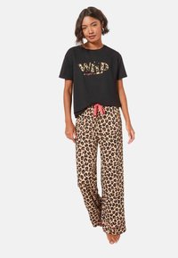 Fekete, rövid ujjú póló "WILD" felirattal leopárdmintával; leopárdmintás, széles szárú nadrág piros húzózsinórral és puha anyagtextúrával.