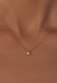 Gold chain necklace featuring a small, square pendant set with four clear stones, resting against a skin-toned background.