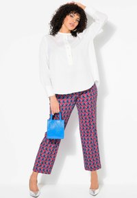 Blusa blanca con una tapeta de botones, combinada con pantalones rojos y azules con estampado. Para completar el look, lleva un pequeño bolso azul y tacones plateados.