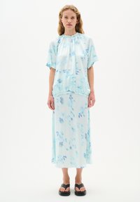 Ljusblå, flödande klänning med elastisk nederkant, korta ärmar och abstrakta blå mönster; kombinerad med svarta, platta sandaler.