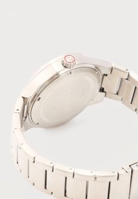 Ασημένια μπάντα και πίσω θήκη από ανοξείδωτο ατσάλι ρολογιού χειρός με κόκκινη λεπτομέρεια στο κουρδιστήρι, σε λευκό φόντο.