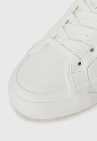 Baskets blanches avec une tige en synthétique lisse, un bout arrondi, des lacets plats et une semelle en caoutchouc texturée avec de subtils détails de couture.