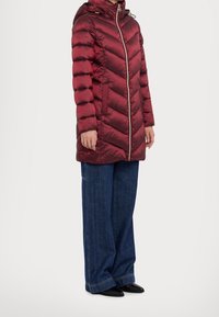 Punainen puhvitakki hupulla, jossa on viistekuvio, kultainen vetoketju ja sivutaskut, yhdistettynä löysiin sinisiin farkkulyhennelmiin.