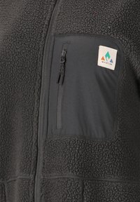 Mustat fleece-takit, joissa on teksturoitu pinta. Varustettu vetoketjullisella rintataskulla ja logopatchilla. Sileät kangaspäällysteet sivuilla.