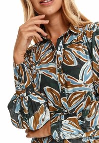 Dlouhá blůza s dlouhým rukávem s vícolor designem listů v modré, hnědé a krémové barvě. Zapínání na knoflíky vpředu a nařasené nabírané rukávy z jemné tkaniny.