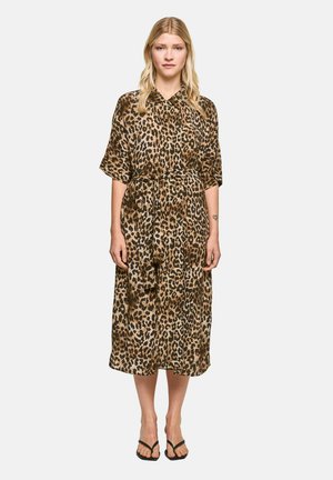 Woman with long blonde hair wears a loose, knee-length leopard print dress with a tie belt and black sandals, standing facing forward.
