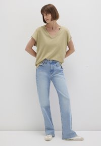 Olive green, short-sleeve V-neck top paired with light blue, straight-leg jeans. The fabric is soft and slightly textured; shoes are light beige.