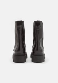 Czarne skórzane botki za kostkę z masywną gumową podeszwą, z elastycznymi wkładkami po bokach i pętelką przy pięcie. Gładka faktura, elegancki design.