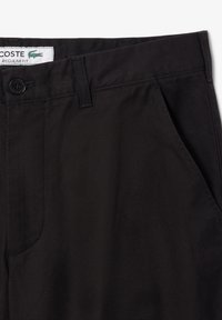 Pantaloni neri in fit regolare con chiusura a bottone, tasche laterali e tessuto testurizzato. Presenta il logo Lacoste sull'etichetta in vita.