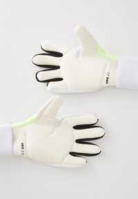 Hvite målvogterhansker med svarte fingertupper og grønn detalj ved håndleddet; laget av teksturert latex og stoffmaterialer.