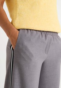 Pantalones grises ajustados con cintura elástica y bolsillos laterales, que presentan una raya vertical en blanco y negro a lo largo de las costuras exteriores.