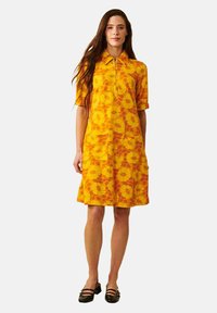 Keltainen lyhythihainen mekko, jossa on kukkakuosi, kaulus, kaksi etutaskua ja rento istuvuus, valmistettu kevyestä kankaasta.