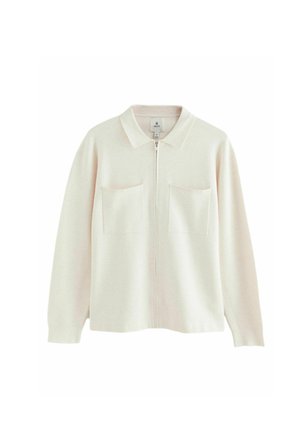 Veste zippée beige clair en tissu doux, avec un col, deux poches avant et des manches longues. Design simple avec des accents minimaux.