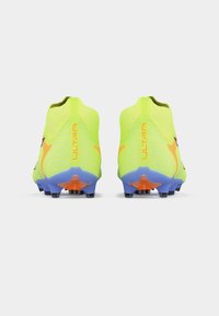 Νεον κίτρινα ποδοσφαιρικά παπούτσια με μοβ και πορτοκαλί σόλες, φαίνονται από πίσω, εμφανίζοντας το κείμενο "ULTRA" στις φτέρνες.