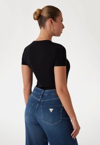 Un tricou slim negru asortat cu blugi din denim albastri. Blugii au un logo triunghiular pe buzunarul din spate și o textură netedă, cu o talie medie.