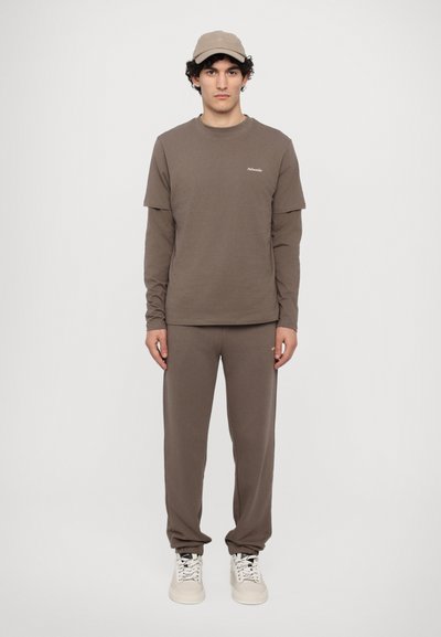 T-shirt à manches longues marron associé à un sweat de jogging assorti et à une casquette. Le tissu est lisse, avec un design minimaliste et un détail de logo subtil.