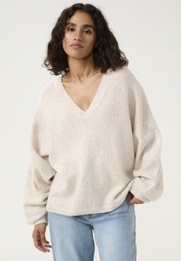 Pull en laine oversize beige clair avec un col en V, finition texturée et légers éclats de détails métalliques. Manches amples.