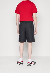 Červená košile s krátkým rukávem, černé kraťasy s elastickým pasem, bílý znak Nike, a černé boty s červenými akcenty, nošeny s bílými ponožkami.