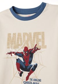 Camiseta beige con cuello redondo azul. Presenta un gráfico de Spider-Man en rojo y azul, con "MARVEL" impreso en dorado arriba.