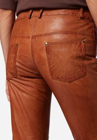 Bruine leren broeken met een glanzende textuur, voorzien van twee achterzakken en zichtbare stiksels. Het ontwerp heeft een stevige tailleband.