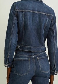 Dark blue denim jacket with a fitted design, visible stitching, two back pockets, and button accents, shown from the back.
