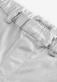 Metalliskt silverfärgade byxor med en glänsande yta. Har en elastisk midja och sömnadsdetaljer vid fickorna, märkta med "AllSaints."