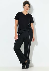 Czarny t-shirt z dekoltem w serek z subtelną grafiką oraz czarne spodnie z białymi paskami po bokach. Noszone z czarnymi tenisówkami na jednolitym tle.