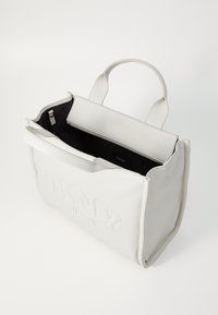 Weißer Leder-Tote mit geprägtem "DKNY"-Logo, Reißverschlussverschluss, doppelten oberen Griffen und einer kontrastierenden schwarzen Innenauskleidung.
