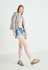 Jachetă bomber cu model floral, căptușită, în alb, roz și verde; combinată cu pantaloni scurți din denim distrus și pantofi sport maroni cu dungi albe.