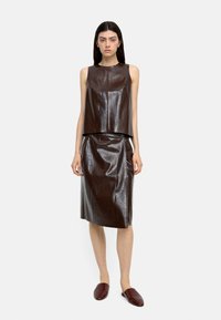 Brązowy skórzany top bez rękawów i pasująca spódnica o ołówkowym kroju z gładką teksturą. Ubranie ma subtelny połysk i dopasowany krój. Brązowe klapki.