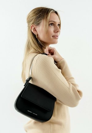 Sac à main noir en cuir, de forme arrondie, texture lisse, matériel en argent, et rabat à l'avant. Porté de manière décontractée à l'épaule.
