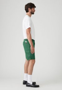 Grønne bomuldsshorts med lige pasform, flad front og sidelommer, parret med en hvid crew-neck t-shirt og sorte loafers.