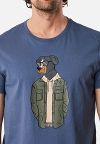 Blue cotton t-shirt featuring a graphic of a Rottweiler wearing sunglasses and a green jacket over a beige hoodie.