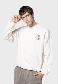 Εξαιρετικά μεγάλος κρεμ φούτερ με υφή, διαθέτοντας ένα πολύχρωμο γραφικό σχέδιο με μια φοινικιά στην αριστερή περιοχή του στήθους.