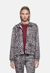 Fleece-Jacke mit Leopardenmuster in Lavendel- und Burgundertönen mit Frontreißverschluss, elastischen Bündchen und Seitentaschen, kombiniert mit einem passenden Oberteil.