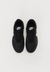 Sorte Nike sneakers med tekstureret stof, rund tå, hvidt logo og flade snørebånd. Glat sål med subtile accenter. Set oppefra.