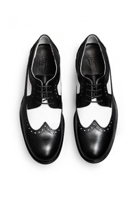 Chaussures en cuir noir et blanc avec un design à bout d'aile, des bords festonnés, des accents perforés et un système de laçage classique.