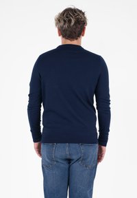 Maglione lavorato a maglia blu navy con maniche lunghe e colletto rotondo, abbinato a jeans blu, visto da dietro. Texture liscia, vestibilità classica.