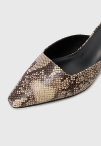 Chaussure à talon aiguille avec un bout pointu dans un motif imprimé serpent marron et crème, arborant un extérieur lisse et texturé ainsi qu'un intérieur noir élégant.