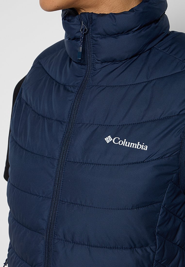 Gilet rembourré bleu marine en matériau synthétique, doté d'un col montant, de coutures verticales et d'une fermeture éclair avec un logo Columbia.