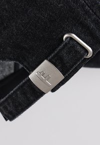 Black denim strap with silver hardware featuring an embossed logo. Textured fabric, sturdy construction, and a clean design.