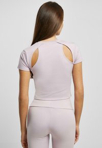 Fialová crop top s krátkymi rukávmi a detailami s výrezmi na chrbte. Hladká, elastická tkanina so priliehavým strihom. V páre s ladnými legínami.