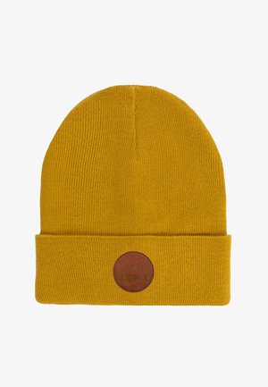Musztardowa żółta czapka dzianinowa z wywiniętym mankietem, z okrągłą brązową skórzaną naszywką z wytłoczonym wzorem. Miękka faktura i prosty design.