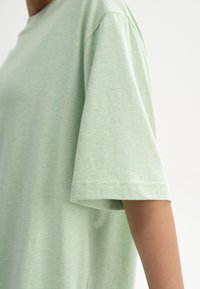 Hellgrünes, kurz�ärmliges T-Shirt aus weichem Stoff. Verfügt über einen lockeren Schnitt mit einem runden Halsausschnitt und sichtbaren Nähten an den Ärmeln.