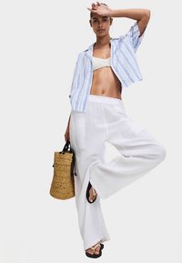 Bílé kalhoty s širokými nohavicemi z texturované látky, modrobíle pruhovaná košile s krátkým rukávem a pletená taška. Sandály s černými pásky.
