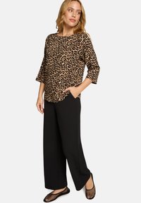 Oberteil mit Leopardenmuster und Dreiviertelärmeln, kombiniert mit weitem schwarzen Hosen. Strukturierte schwarze Ballerinas vervollständigen den Look.