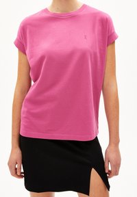 T-shirt di cotone rosa con maniche arrotolate e piccolo logo ricamato. Indossato con una gonna nera con uno spacco laterale.