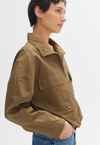 Khaki Bomberjacke mit Reißverschlussfront, hohem Kragen und zwei Fronttaschen, gefertigt aus leichtem Baumwollmix-Stoff.