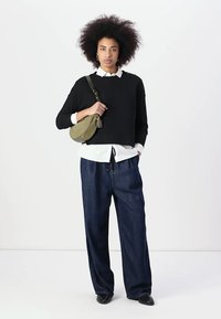 Black cropped sweater layered over a white button-up shirt, paired with loose blue jeans and a green shoulder bag. Black shoes.